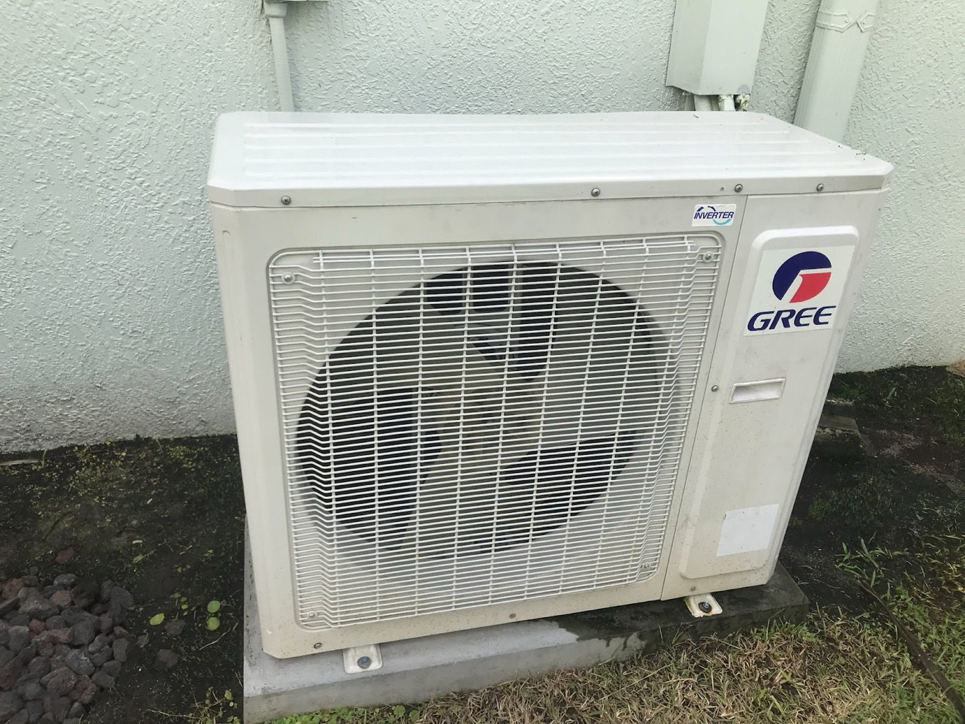 Gree inverter mini-split outdoor unit on a pad beside a stucco wall
